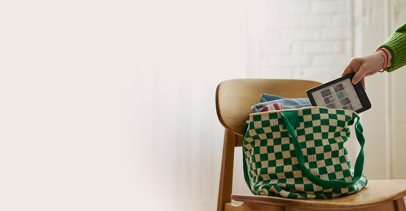 Une main sort une liseuse Kobo Clara Colour d’un sac de livres posé sur une chaise en bois.