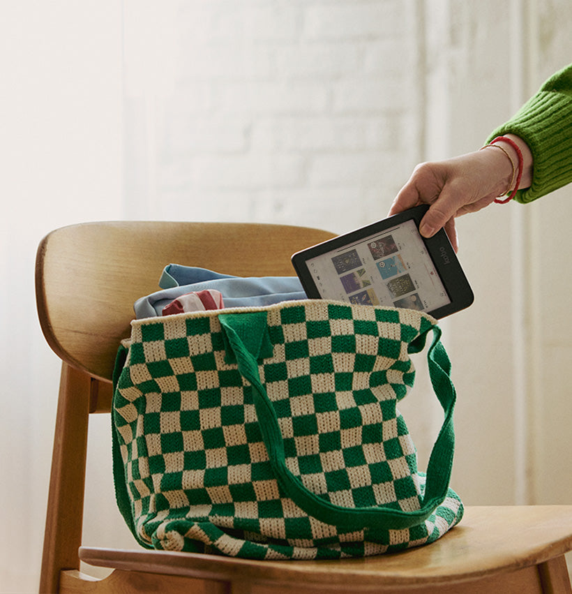 Une main sort une liseuse Kobo Clara Colour d’un sac de livres posé sur une chaise en bois.